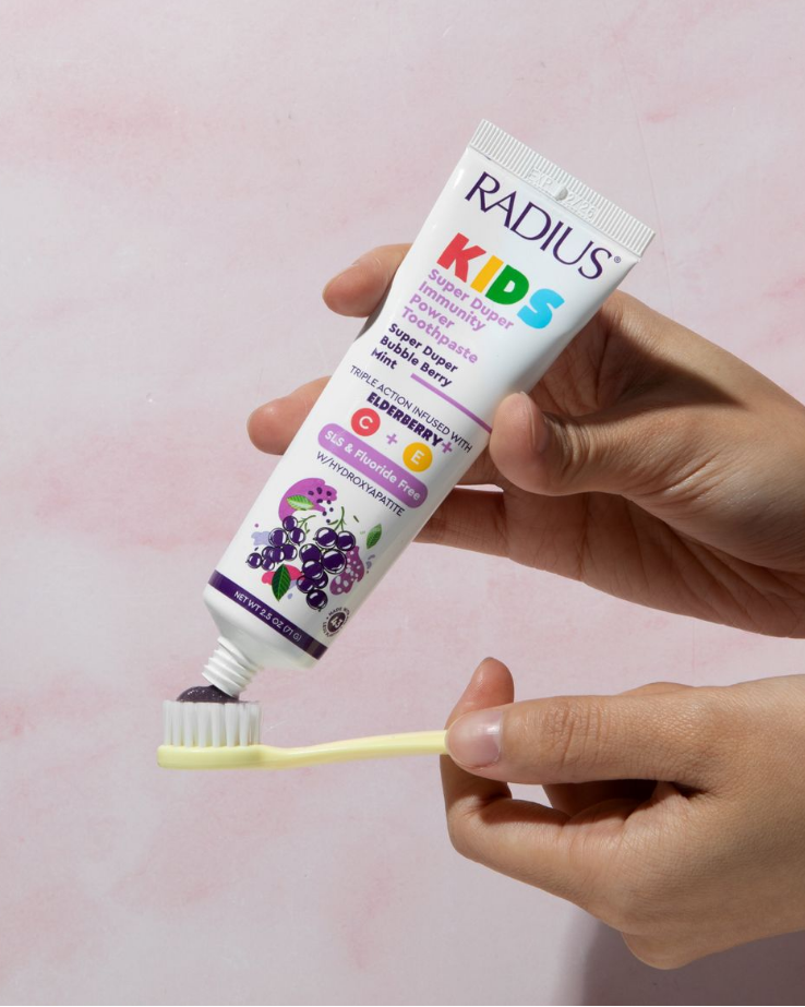 Hand holding a tube of Radius Kids toothpaste with a pink background